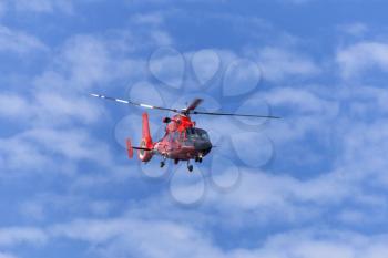 Red rescue helicopter moving in blue sky with blur propeller

