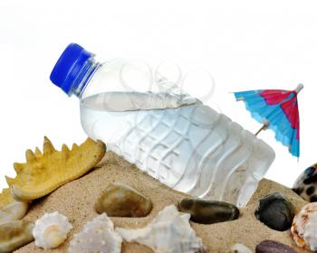 a bottle of cold water and shells on a sand