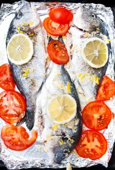 Fresh Sea Bream with lemon, tomatoes and spices on cooking foil