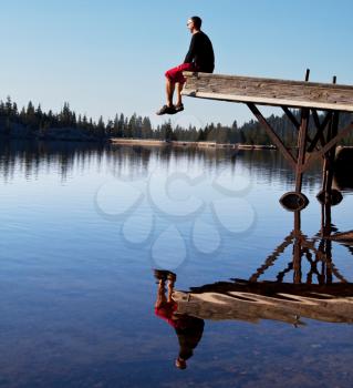 Royalty Free Photo of a Man Sitting on a Dock at a Lake