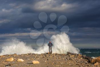 Man standing against the sea on a  pier with big wave beating with splash in a storm weather