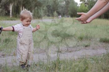 Little boy do his first steps with mother's help in summer park