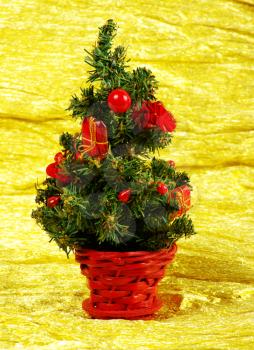 Little decorated christmas tree on golden background with gifts