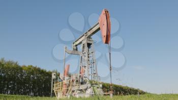 Operating oil and gas well in oil field, profiled against the blue sky.
