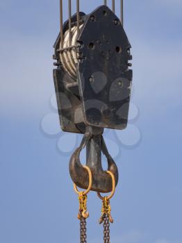 Crane hook with red and white stripes hanging, blue sky in background.