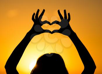 Silhouette of the heart by hands at sunset .