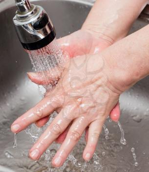 Woman washes her hands under a tap of water .