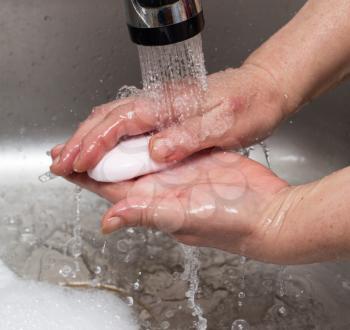 Woman washes her hands with soap under a tap of water .