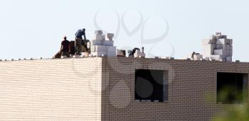 workers work on the roof of a brick house .