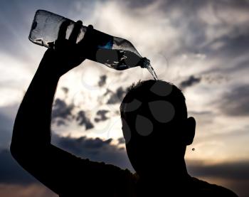 man pours water on his head in the sunset