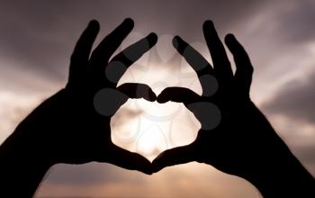 Silhouette of hands in form of heart on the background of sunset