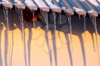 Icicles on the roof of the house at sunset .