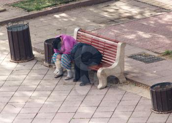Two women homeless sitting in a park on a bench .