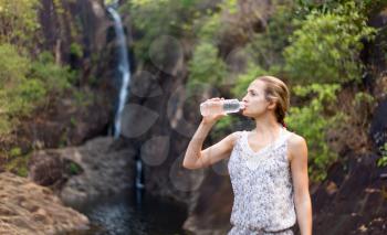 girl drinks water from a bottle on the background of a waterfall.