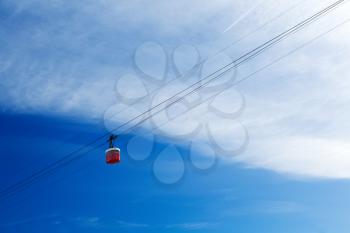Red cable car cabin in the sky with clouds.