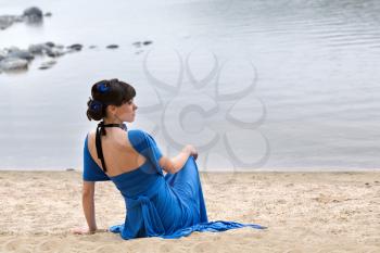 girl in a blue dress sitting on the beach.