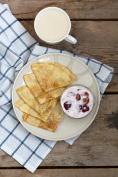 Fried pancakes with jam and a cup of milk on vintage wooden background. Top view