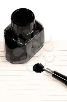 classic black fountain pen on open notebook with ink bottle with stain on page,sepia filter