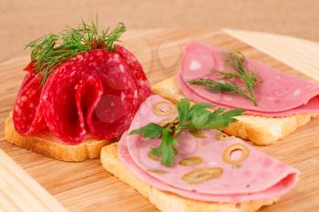 Sandwiches with salami and mortadella on wooden board.