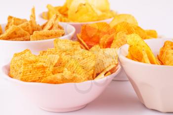 Potato and wheat chips in bowls on gray background.