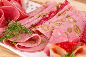 Salami, mortadella and bacon on plate on wooden board.