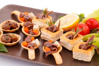 Anchovies in pastries, lemon, tomato, lettuce and basil on brown plate.