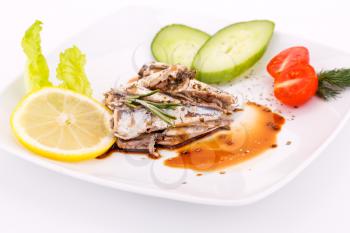 Fish, vegetables and lemon on white plate.