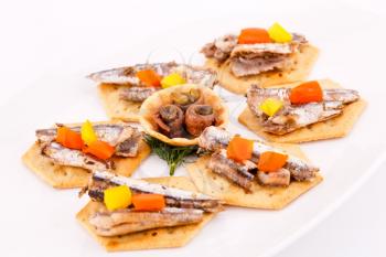 Fish and peppers on crackers  on white plate.