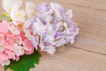 Colorful artificial flowers on wooden background, closeup picture.