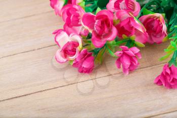 Pink artificial flowers on wooden background, closeup picture.