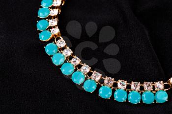 Stylish necklace with colorful stones on black fabric background.