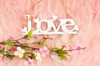 White wooden word love and flowers on pink fur background.