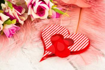 Valentine decoration with red heart and roses on pink feathers background.