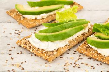 Sandwiches with crackers, cheese, avocado and lettuce on gray wooden background.