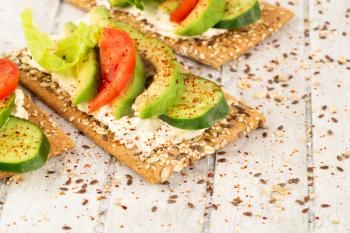 Sandwiches with crackers, cheese, avocado, cucumber, tomato and lettuce on gray wooden background.