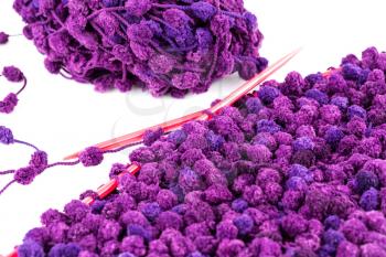 Purple yarn with knitting needles on white background.