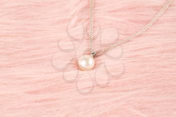 Stylish necklace with pearl on pink fur background.