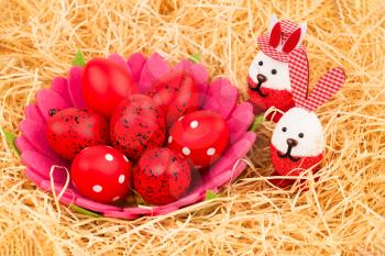 Easter red eggs in basket and bunnies on straw background.