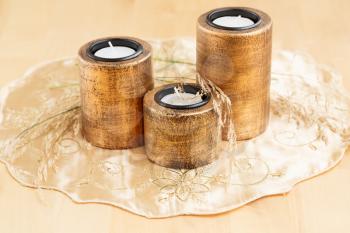 Three brown candle nests with dry plants on golden cloth.