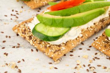 Sandwiches with crackers, cheese, avocado, cucumber, tomato and lettuce on gray wooden background.