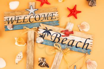 Wooden signs welcome beach, starfish and shells on yellow background.