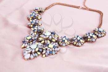 Stylish necklace with colorful stones on pink fabric background.