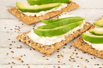 Sandwiches with crackers, cheese and avocado on gray wooden background.