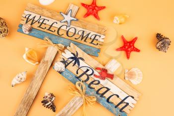 Wooden signs welcome beach, starfish and shells on yellow background.