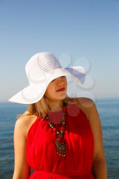 Blond woman in the red dress with the white hat at the beach in Cyprus.