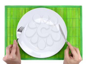 Hands hold fork and knife above plate on bamboo mat. All around Isolated.