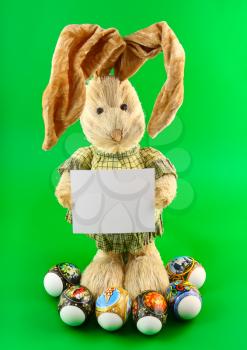 Straw rabbit with blank card in hands on colour background.
