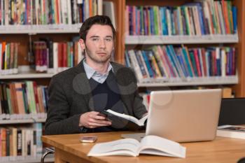 In The Library - Handsome Male Student With Laptop And Books Working In A High School - University Library - Shallow Depth Of Field