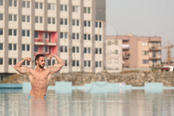 Portrait Of A Very Muscular Sexy Man In Underwear At Swimming Pool Showing Double Biceps Pose