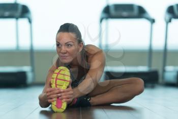 Muscular Woman Stretches At The Floor In A Gym And Flexing Muscles - Muscular Athletic Bodybuilder Fitness Model